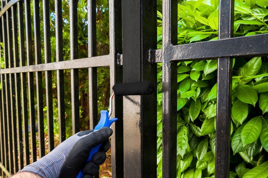 Application d'une peinture noire au rouleau sur une clôture métallique