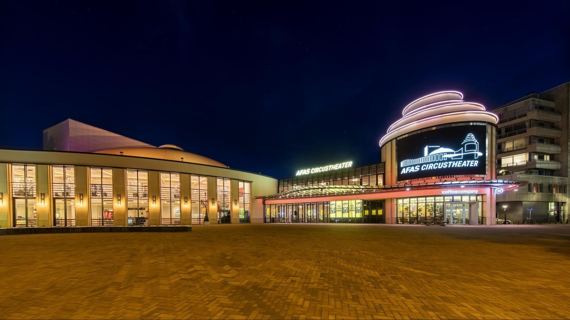 Een groot gebouw met 's avonds een groot scherm ervoor.