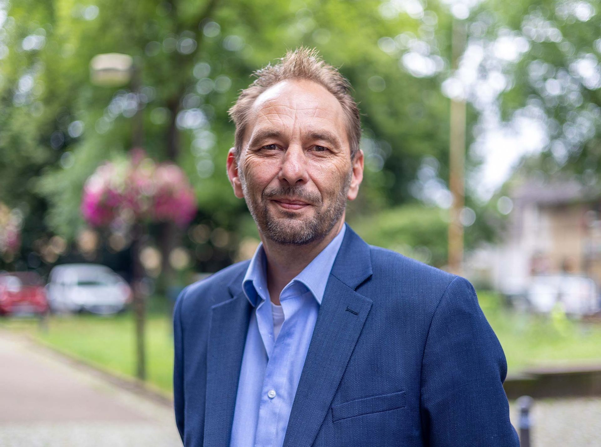 Ein Mann in Anzug und blauem Hemd steht in einem Park.