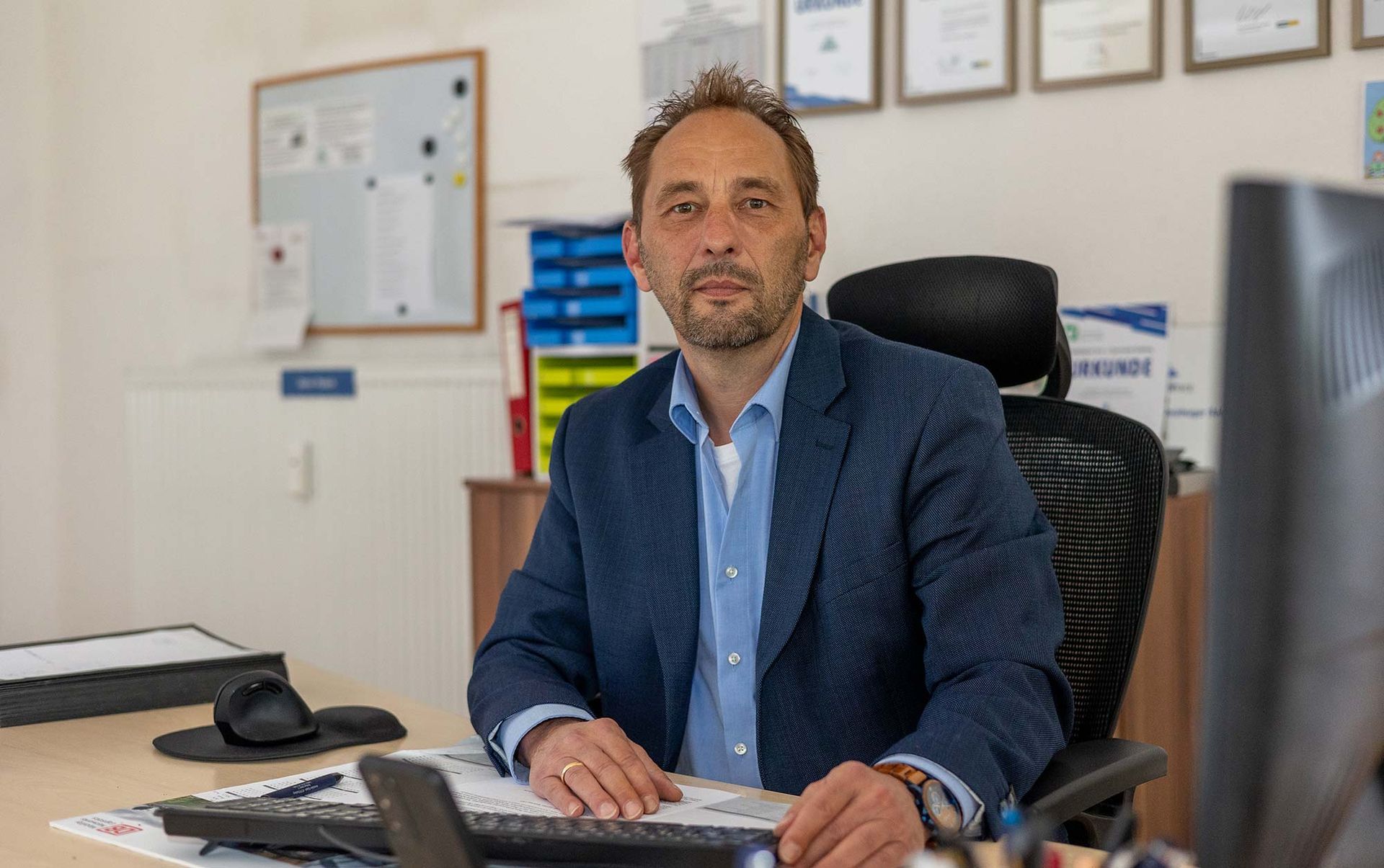 Ein Mann im Anzug sitzt an einem Schreibtisch vor einem Computer.