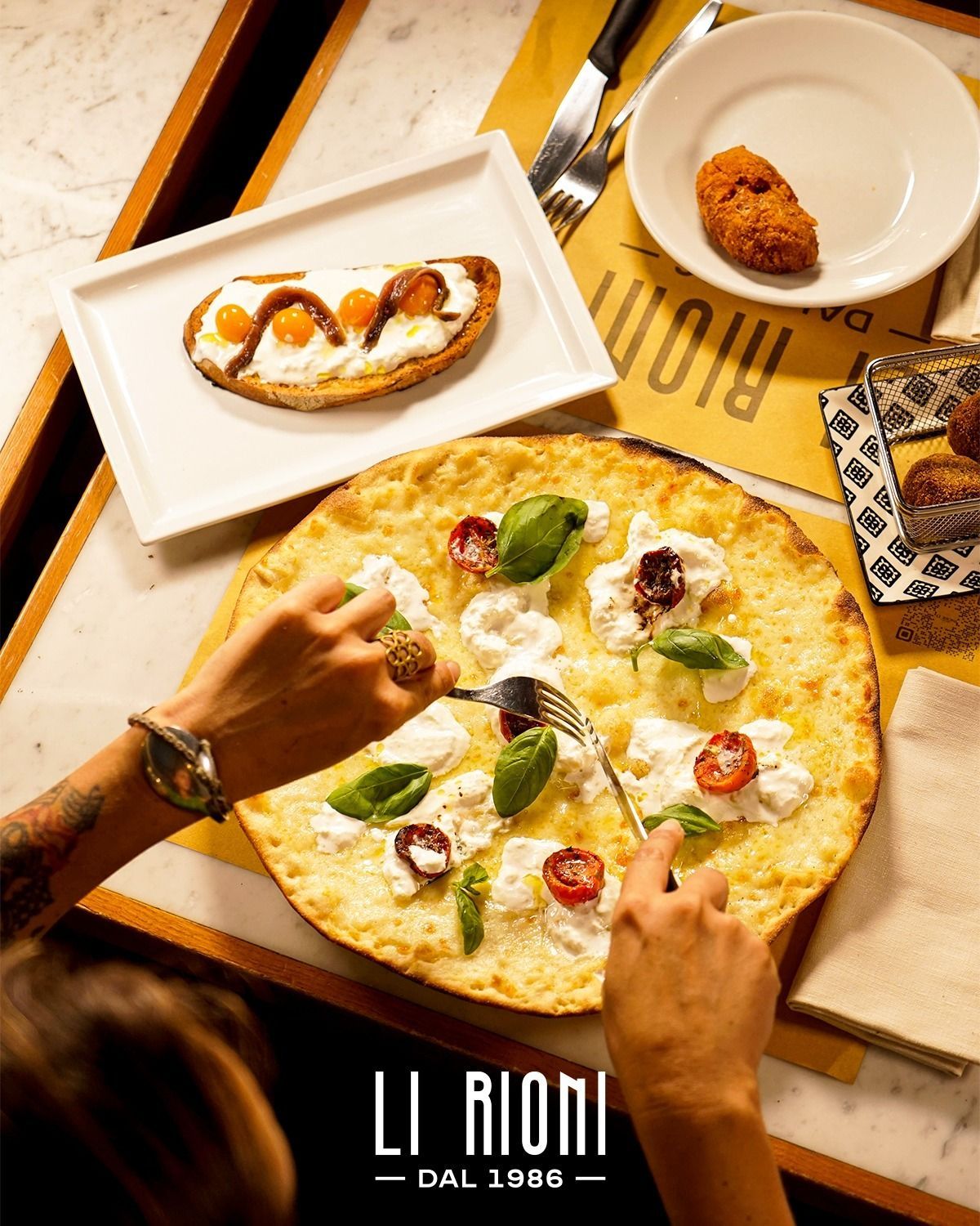 A person is cutting a pizza with a fork in a restaurant called li rioni