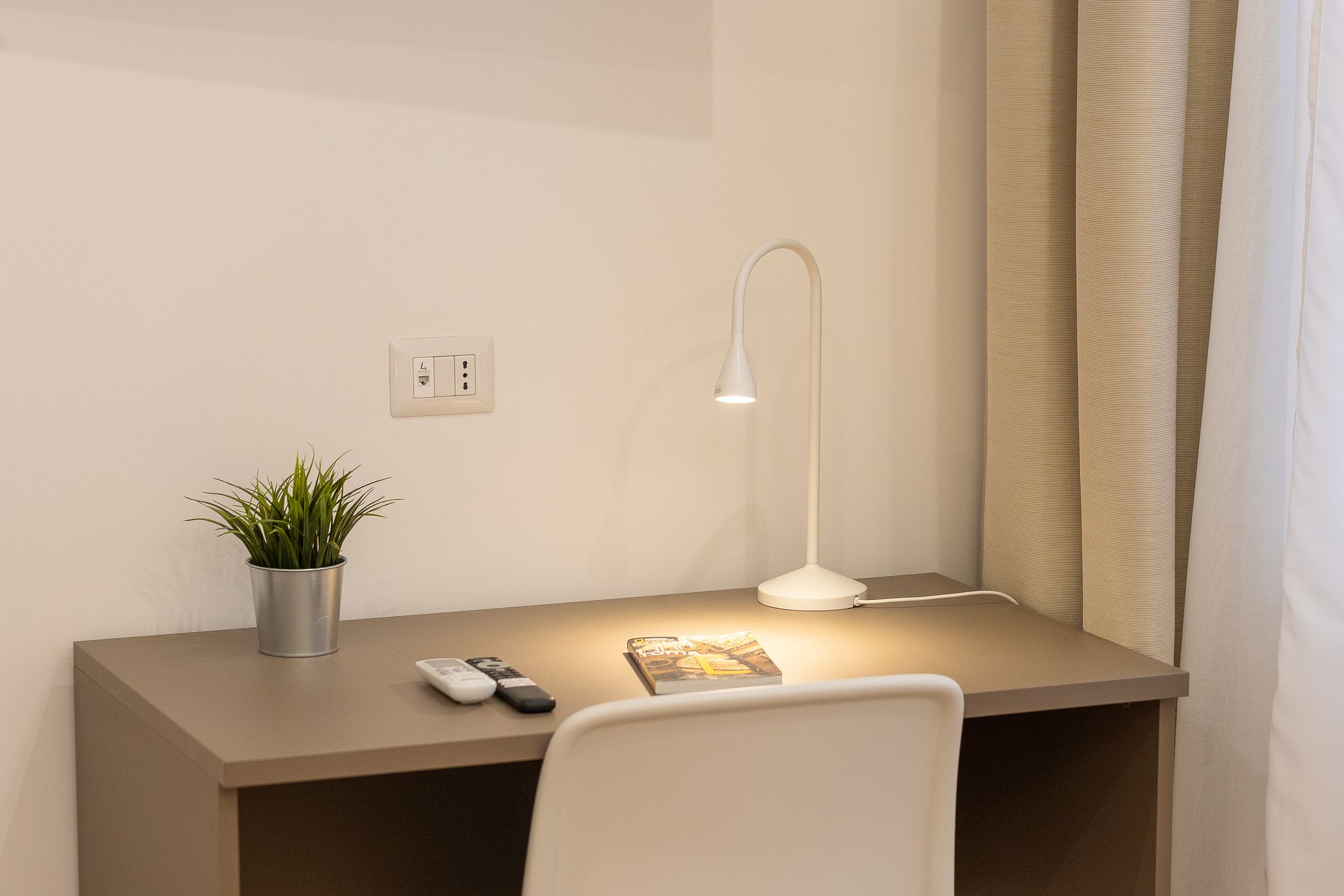 There is a desk with a lamp and a potted plant on it.
