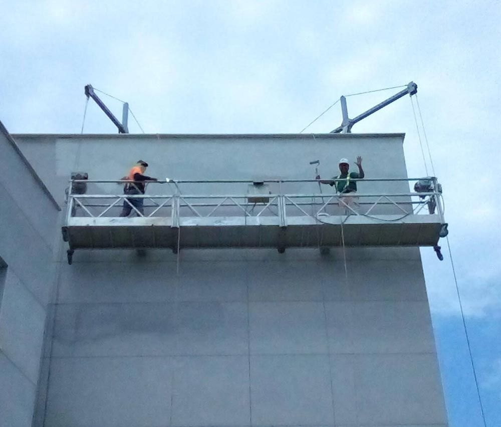 Dos hombres están trabajando en el costado de un edificio en un andamio.