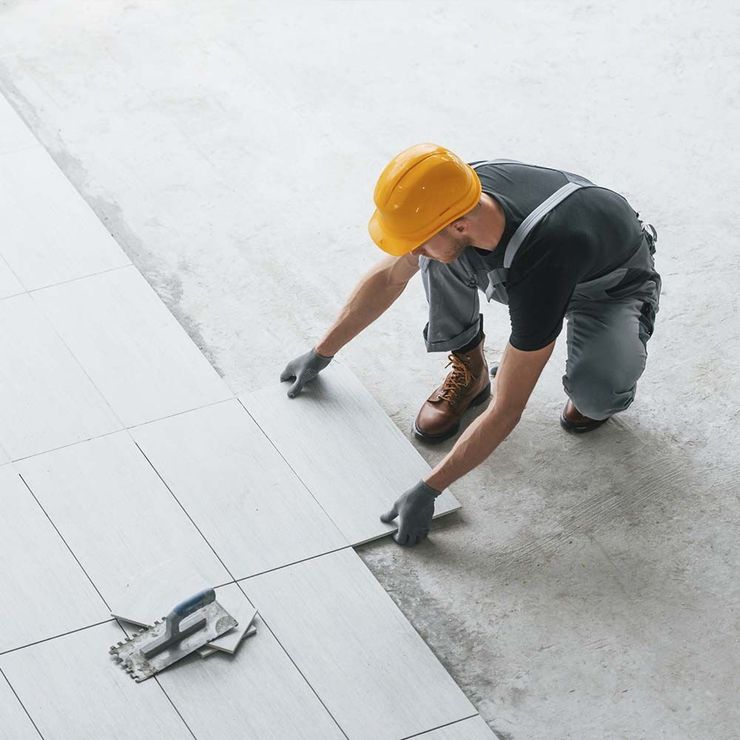 Un hombre que lleva casco y mono está trabajando en un piso de baldosas.