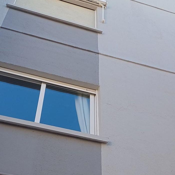 Una ventana en el costado de un edificio con un cielo azul reflejado en ella.
