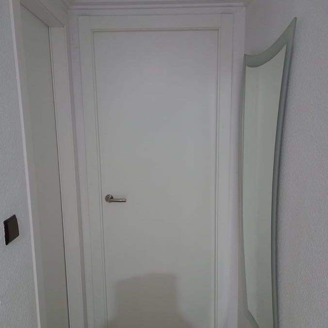 Una puerta blanca está en un pasillo al lado de un espejo.