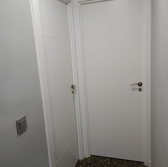 Una puerta blanca está en un pasillo al lado de una pared.