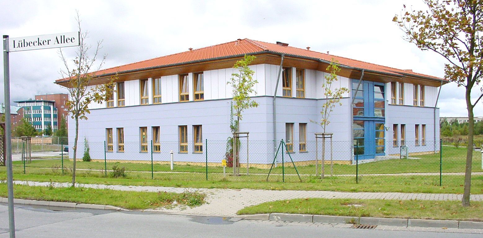 Hellblaues Gebäude mit rotem Dach, davor zwei junge Bäume