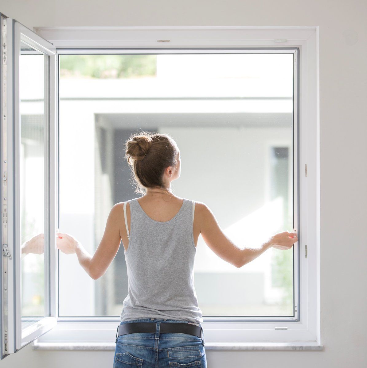 Eine Frau steht im offenen Fenster und greift nach dem Insektenschutzgitter