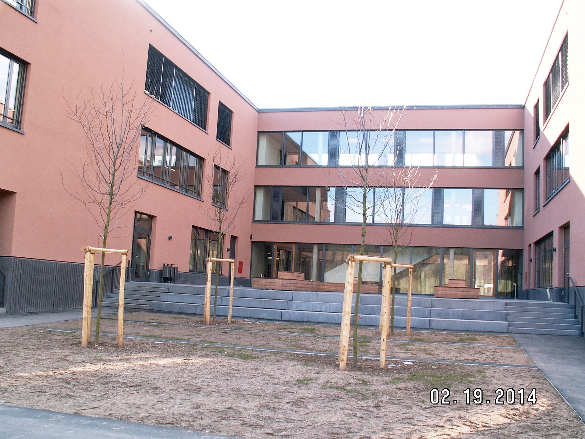 Neubau in Lachsfarben mit vier neu gepflanzten Bäumen davor