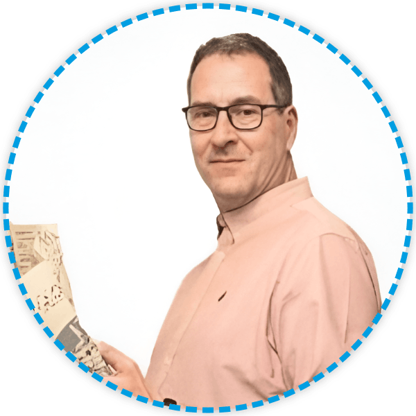 Hombre con gafas y camisa rosa sosteniendo papeles, mirando hacia el espectador, sonriendo levemente.