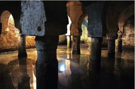 Columnas de piedra subterráneas y techo arqueado reflejados en el agua.