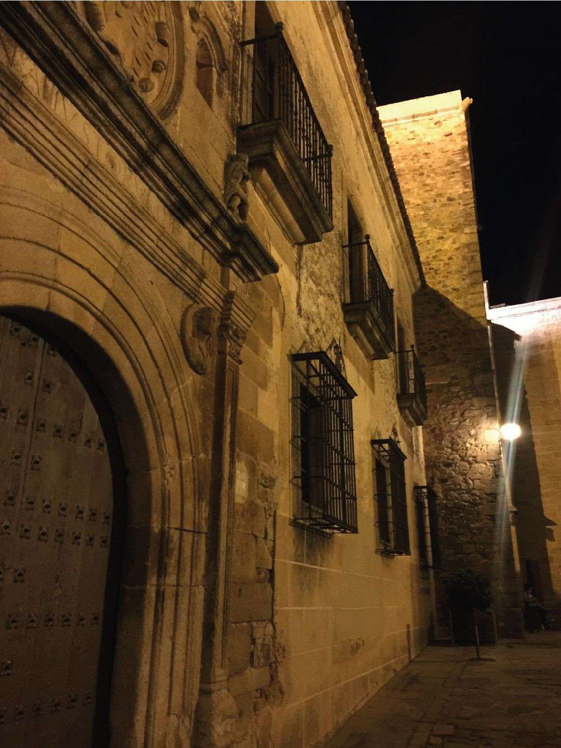 Fachada de edificio de piedra con puerta de arco y ventanas enrejadas, iluminada por la noche.