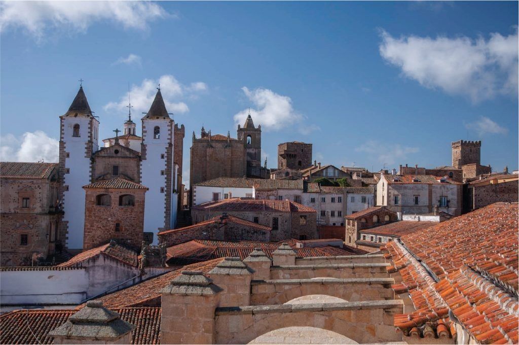 Tejados y torres de Cáceres, España, bajo un cielo azul brillante con nubes dispersas.