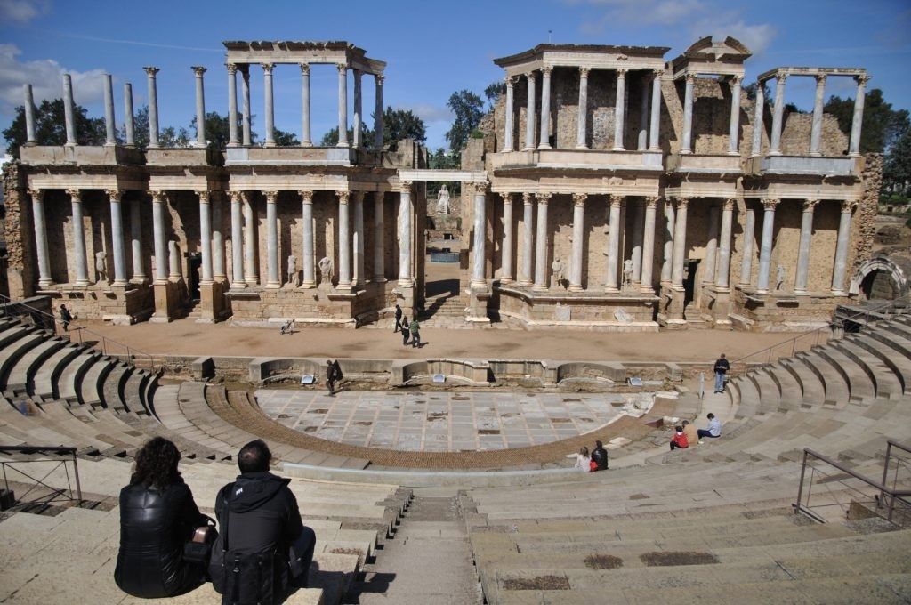 Ruinas del antiguo teatro romano en Mérida, España. La gente se sienta en los escalones de piedra y observa el escenario.