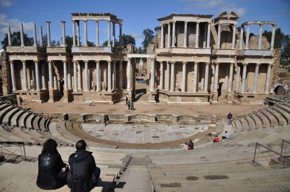 Ruinas del antiguo teatro romano en Mérida, España. La gente se sienta en los escalones de piedra y observa el escenario.