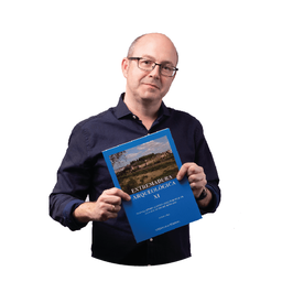 Hombre sosteniendo un libro azul con texto en español titulado “EXTREMADURA ARQUEOLÓGICA XI”.