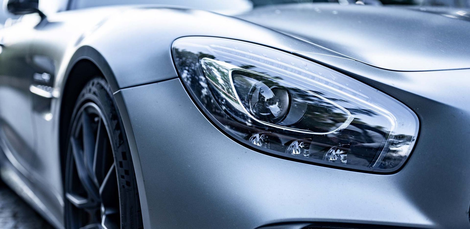 Eine Nahaufnahme des Scheinwerfers eines silbernen Sportwagens.