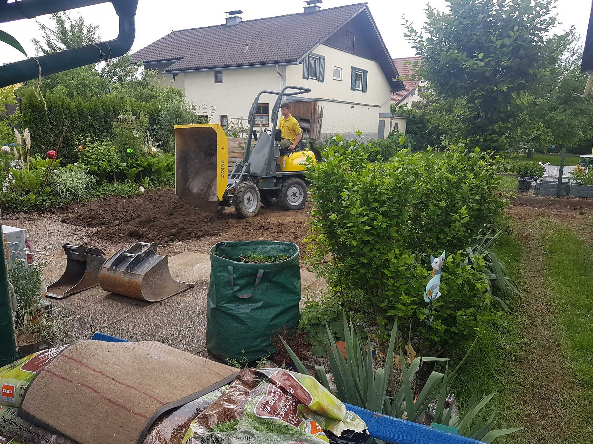 Ein Mann fährt mit einem Bulldozer durch einen Garten vor einem Haus.