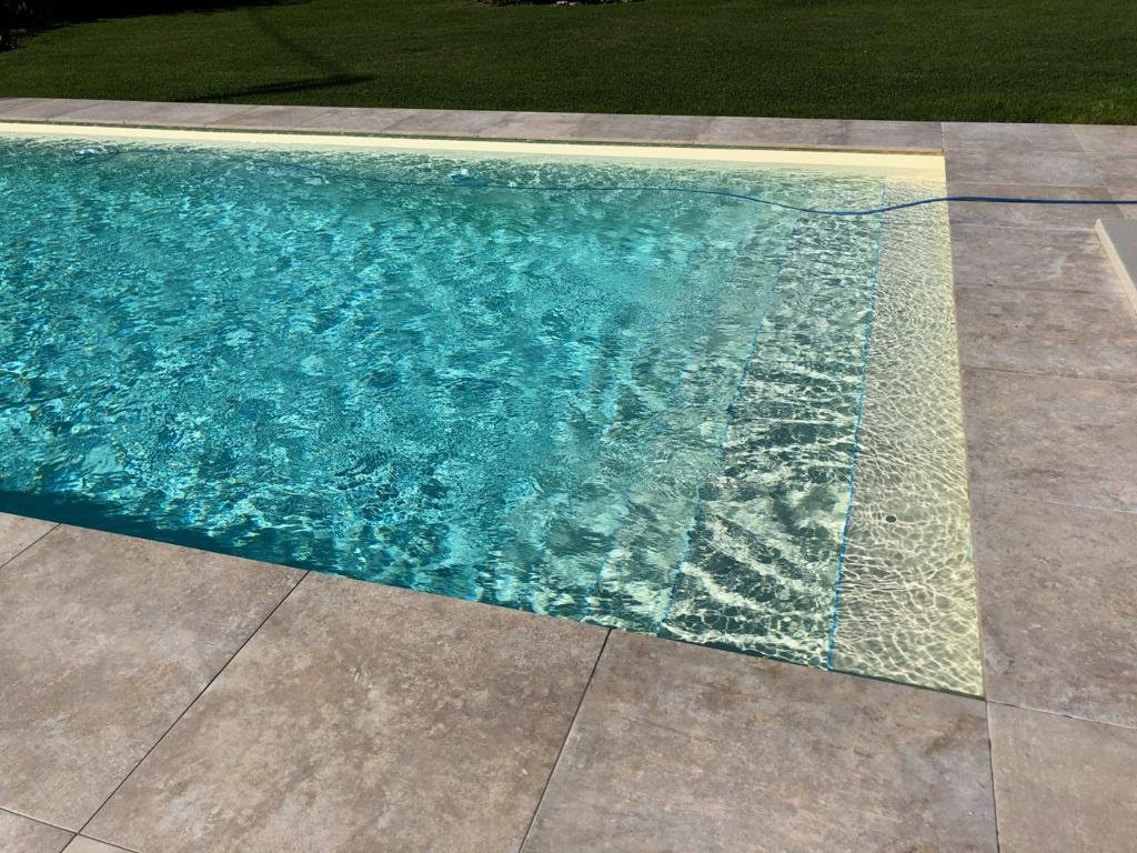 Ein Swimmingpool mit gefliester Umrandung und einer Rasenfläche im Hintergrund.