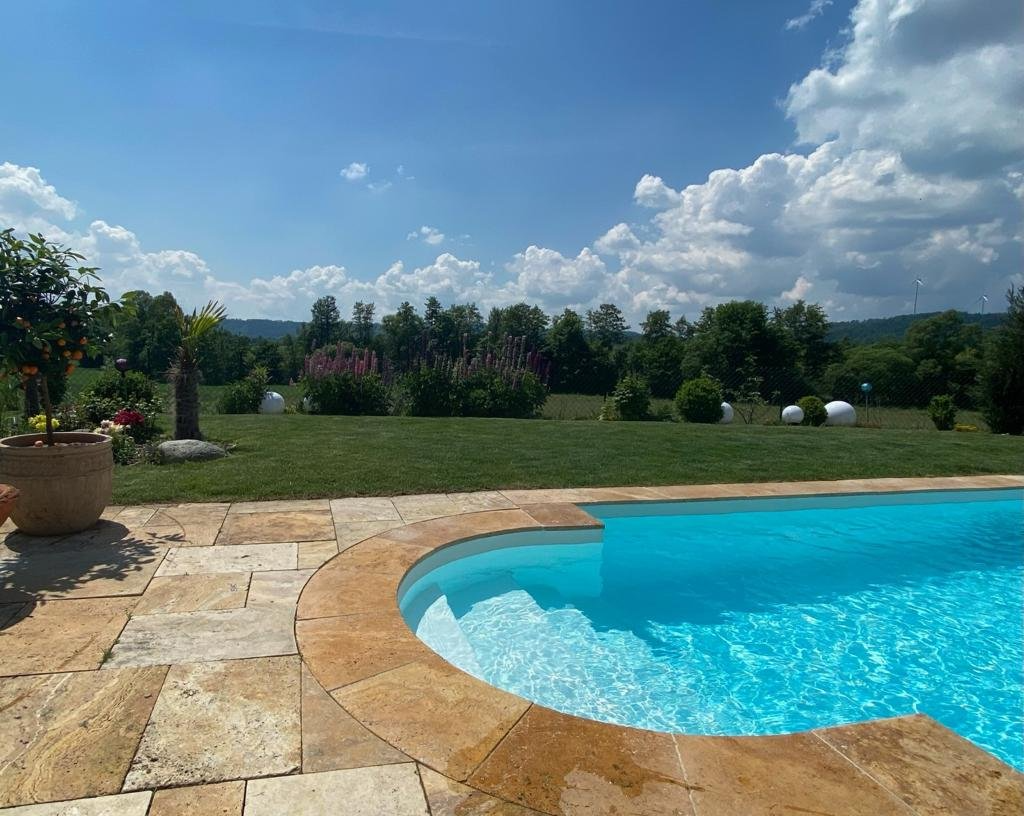 Ein großer Swimmingpool, umgeben von Gras und Bäumen an einem sonnigen Tag