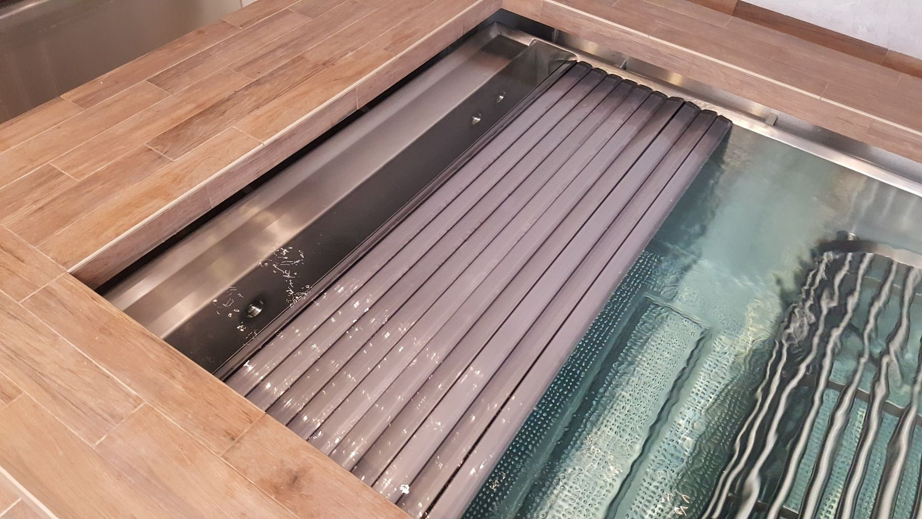 Ein Swimmingpool mit Holzdeck und Edelstahlabdeckung.