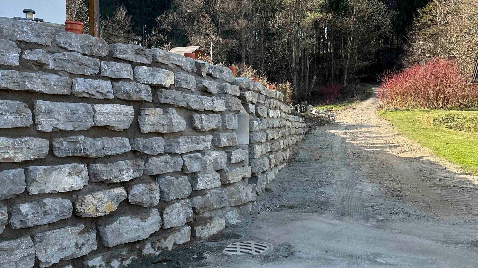 Eine Steinmauer am Rand einer unbefestigten Straße.