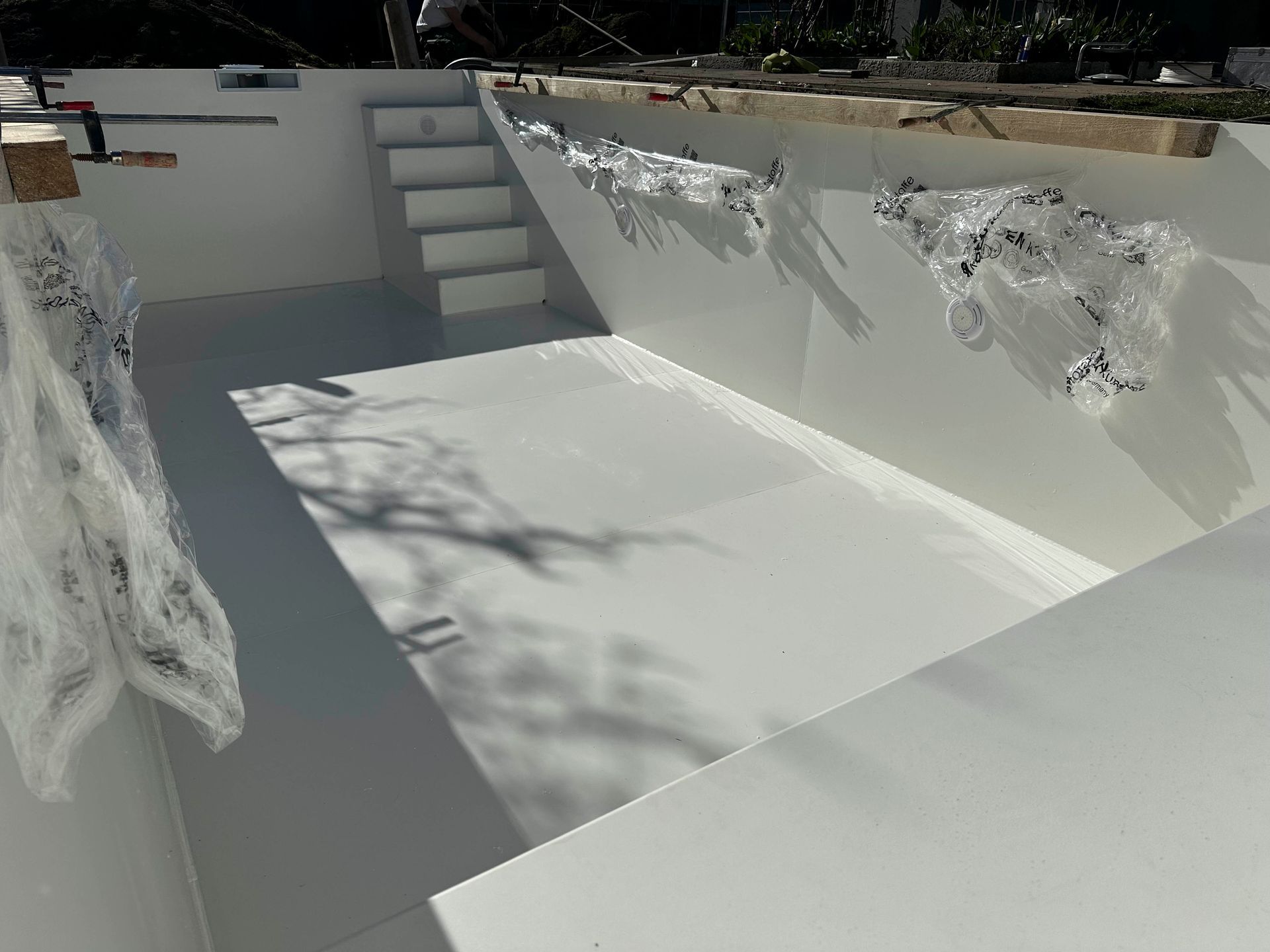 In einen Pool wird eine weiße Treppe eingebaut.
