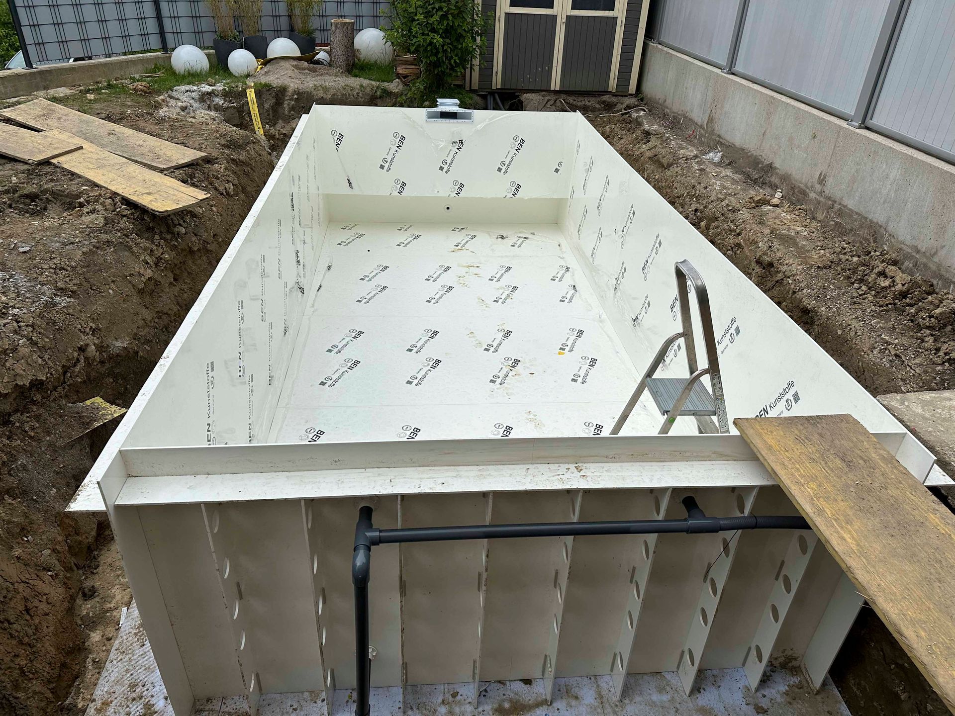 Ein großes weißes Schwimmbecken wird in den Dreck gebaut.