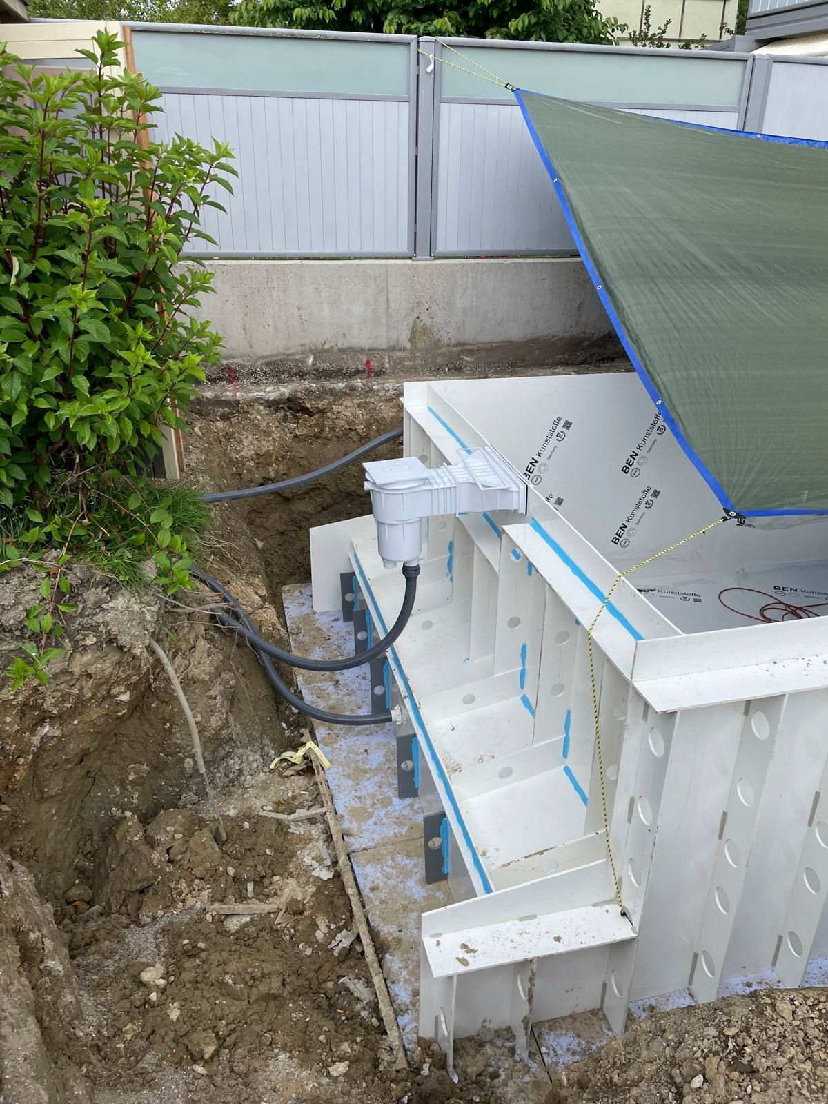 In einem Hinterhof wird ein Swimmingpool gebaut, der mit einer Plane abgedeckt ist.