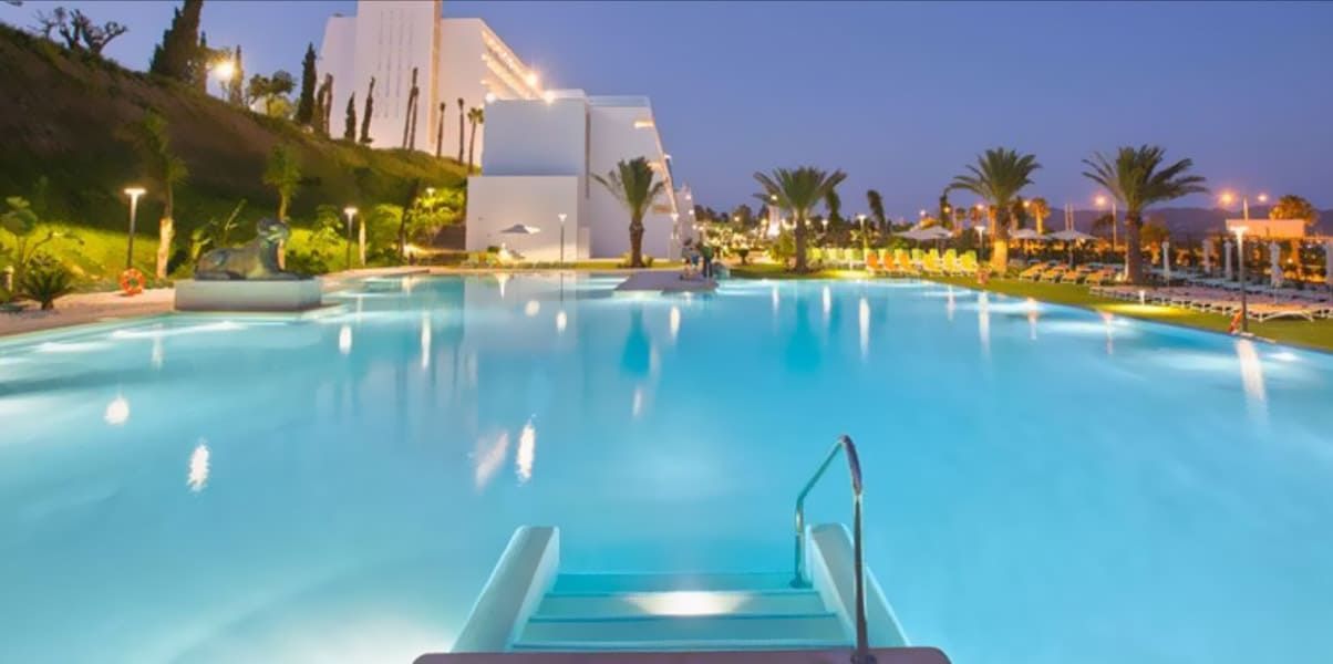 Una gran piscina está iluminada por la noche con escaleras que conducen a ella.