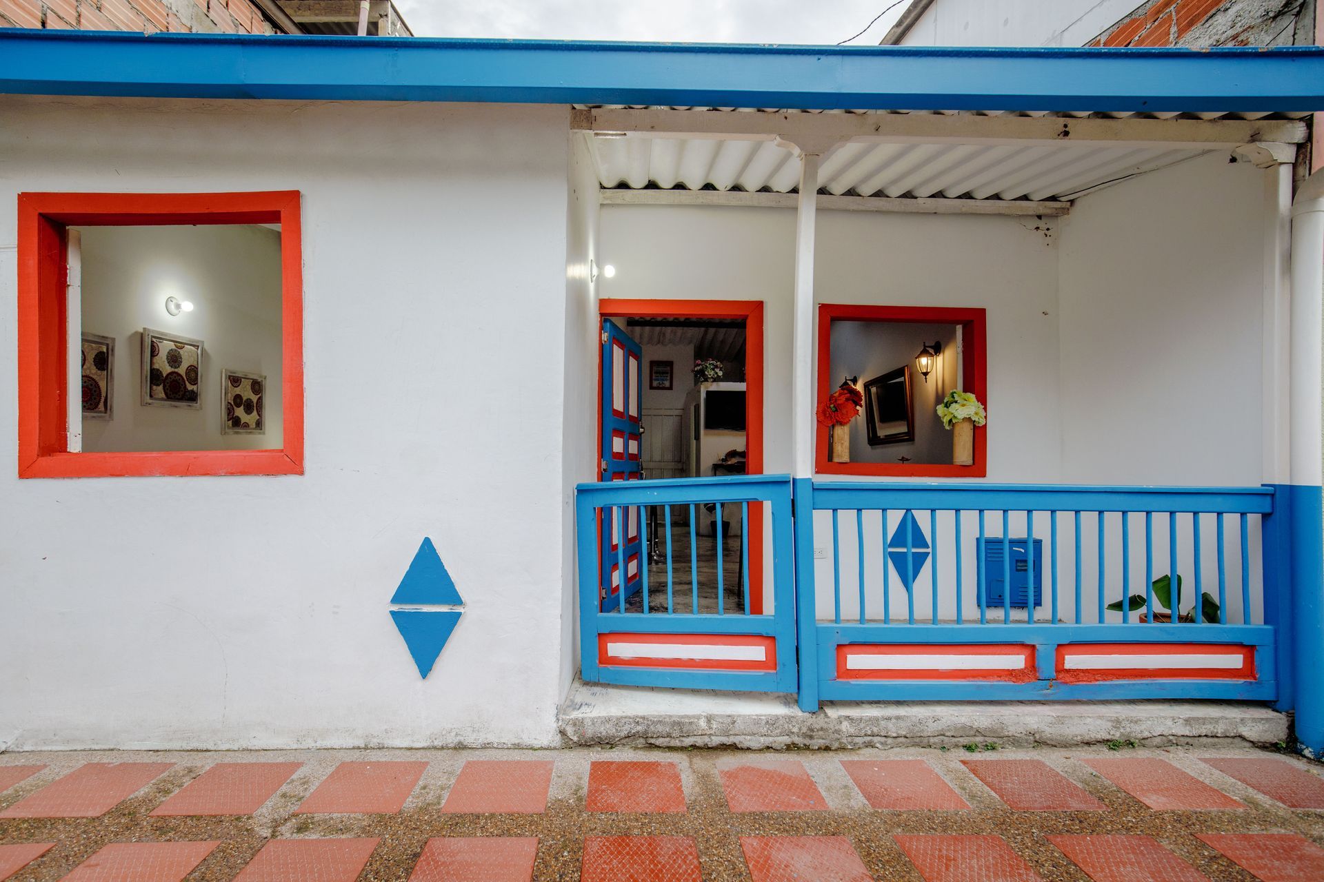 White house with red/blue trim, open door. Blue fence, red-framed windows, brick patio.