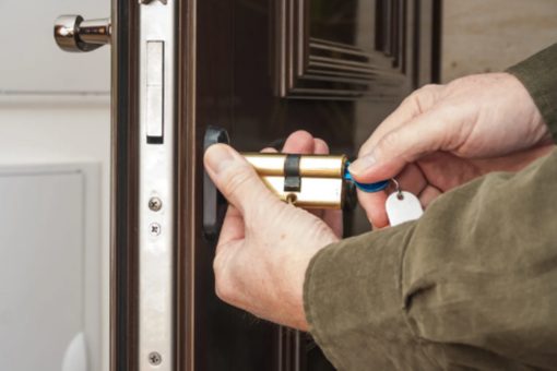 Des mains ouvrent une porte d'entrée avec une clé dans la serrure et un porte-clés bleu.