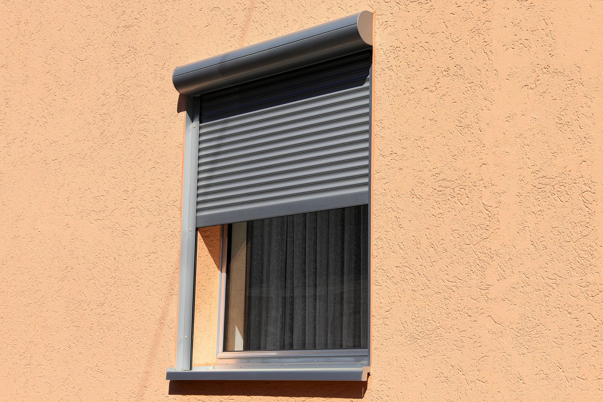 Fenêtre entrouverte avec volet roulant gris sur un mur en stuc couleur pêche