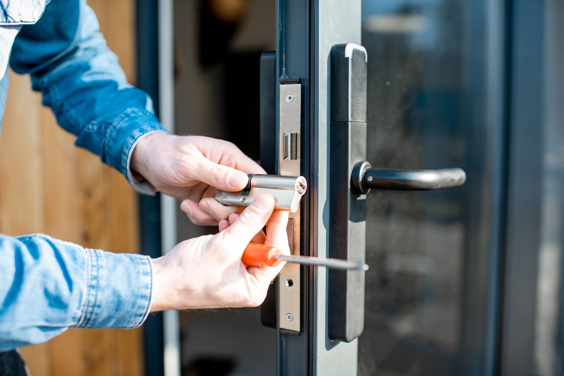Mains installant une serrure de porte argentée sur une porte vitrée à l'aide d'un tournevis