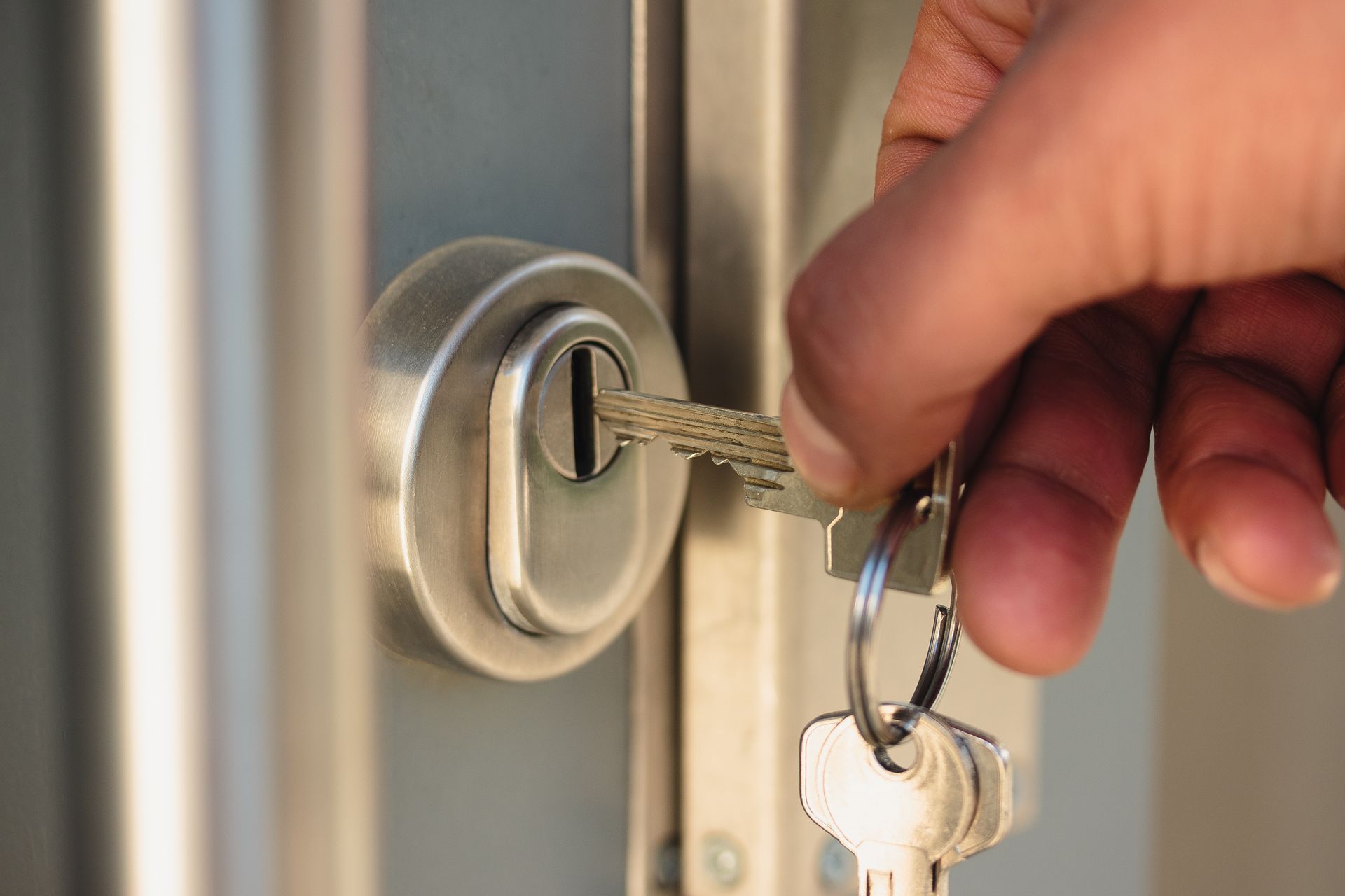Une main insère une clé dans une serrure de porte argentée et tient un porte-clés.