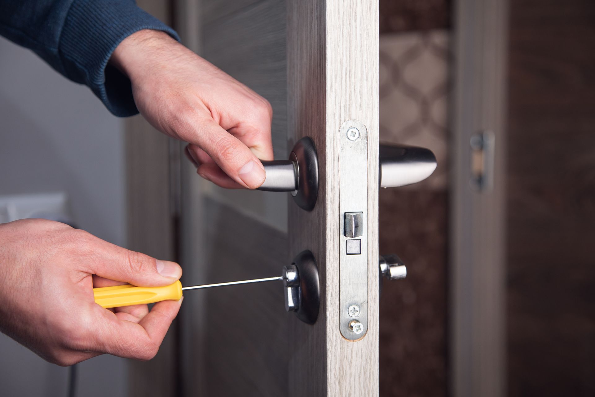 Des mains utilisent un tournevis pour déverrouiller une poignée de porte en bois