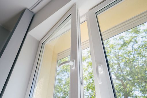 Fenêtre blanche ouverte laissant entrer le soleil et donnant sur des arbres verts à l'extérieur