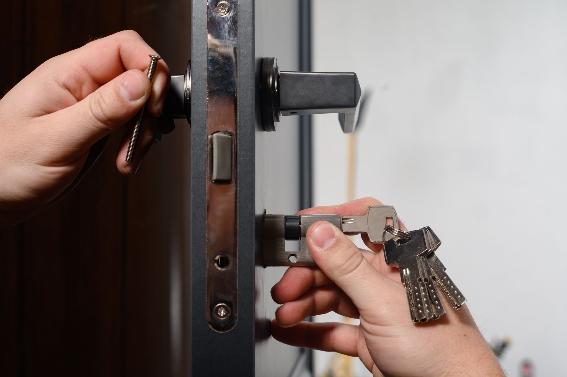 Gros plan sur des mains insérant une clé dans une serrure de porte tandis qu'une autre main tient un porte-clés.