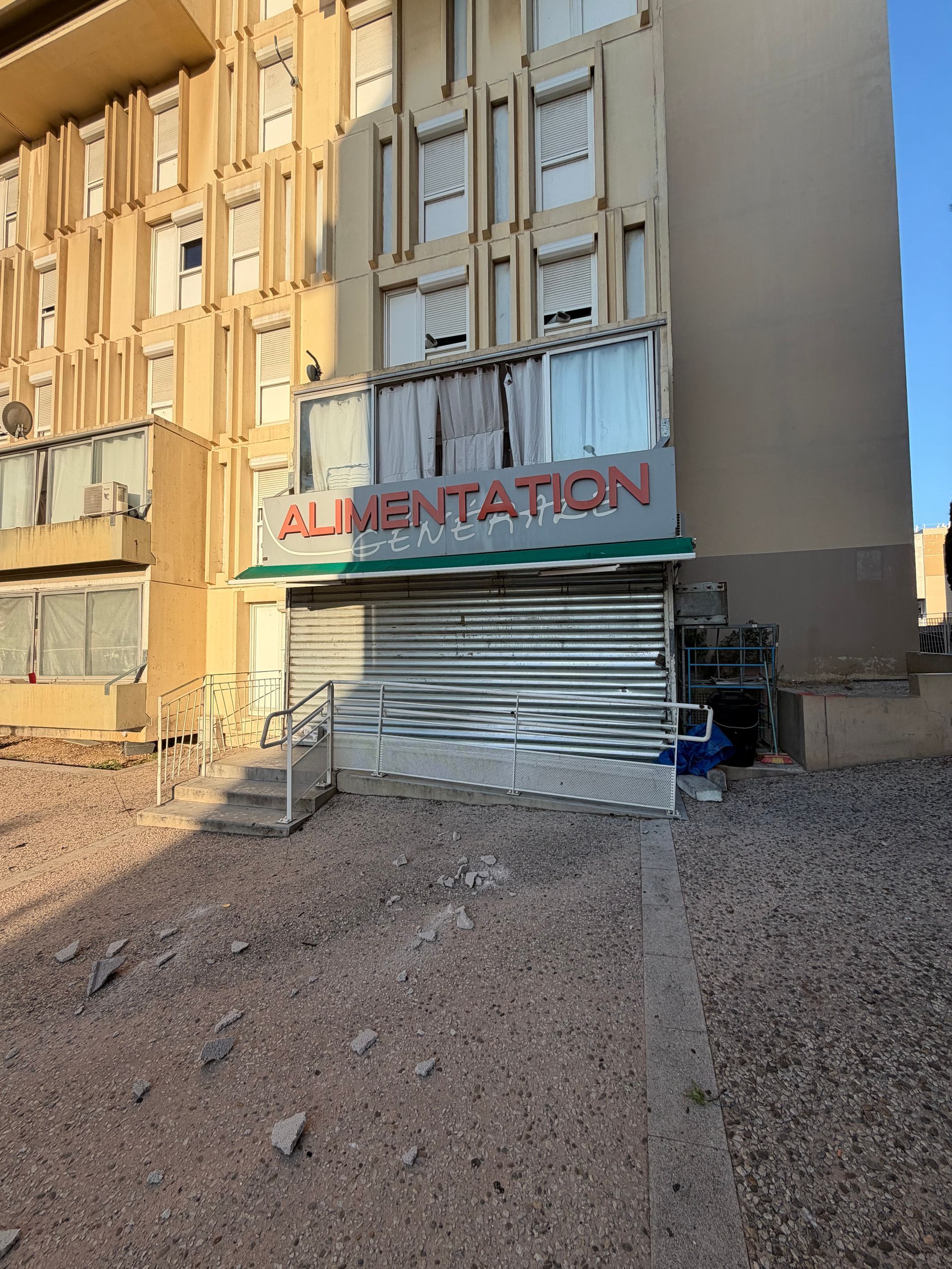 Façade de magasin abandonnée avec un volet métallique et une enseigne indiquant ALIMENTATION sous des fenêtres condamnées.