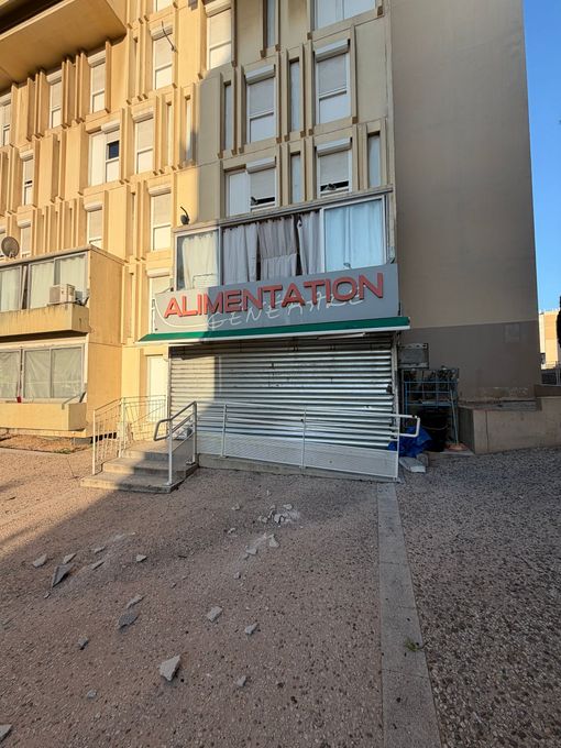 Façade d'immeuble endommagée, fenêtres condamnées et une enseigne au-dessus d'une devanture de magasin fermée.