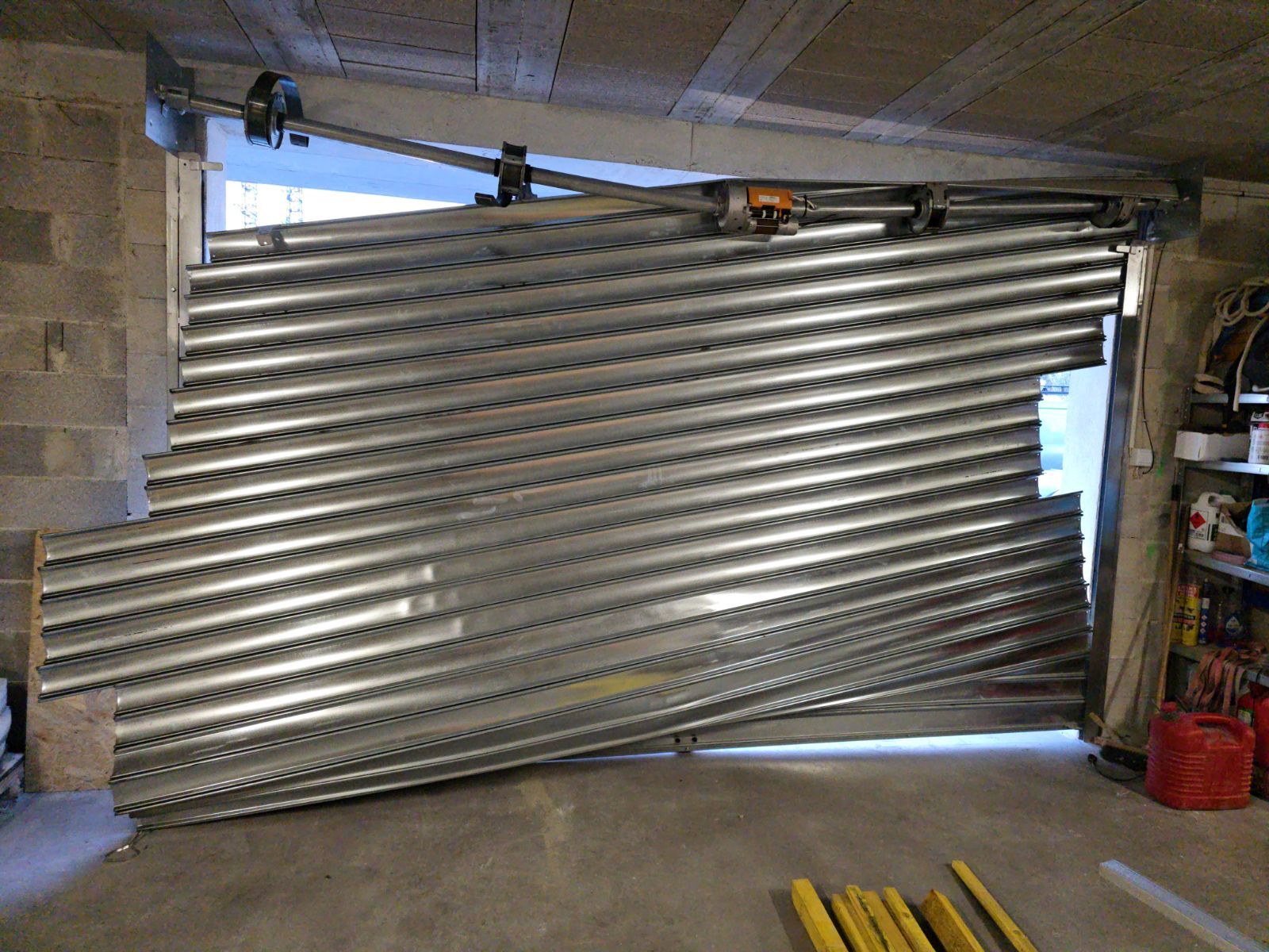 Porte de garage métallique partiellement ouverte et tordue vers l'intérieur, bloquant l'accès à un atelier