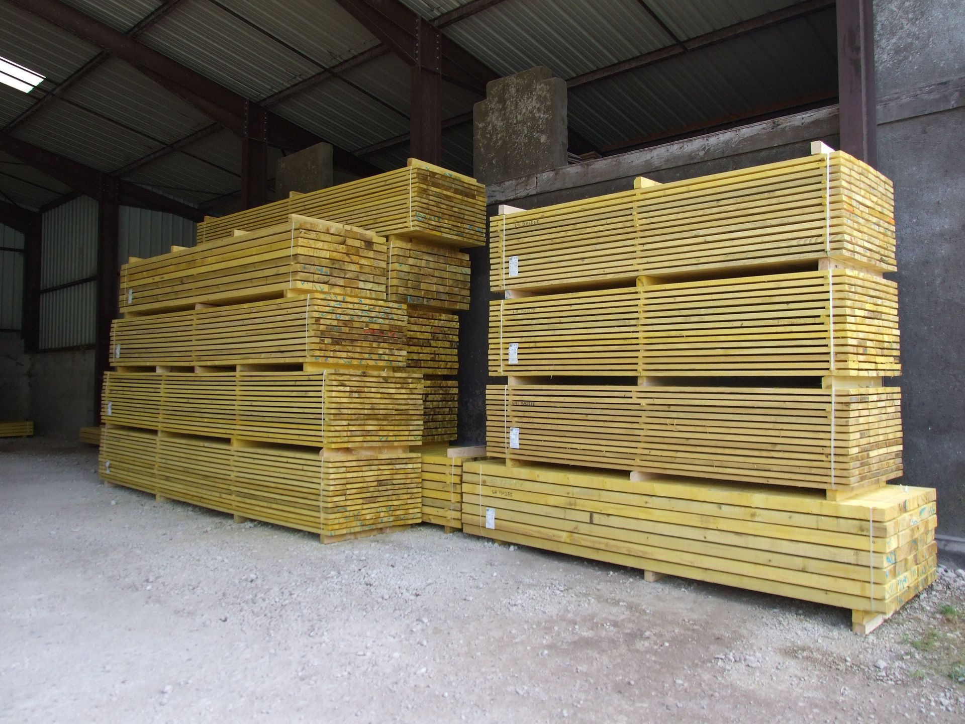 Planches de bois empilées sur un sol en béton dans un atelier.