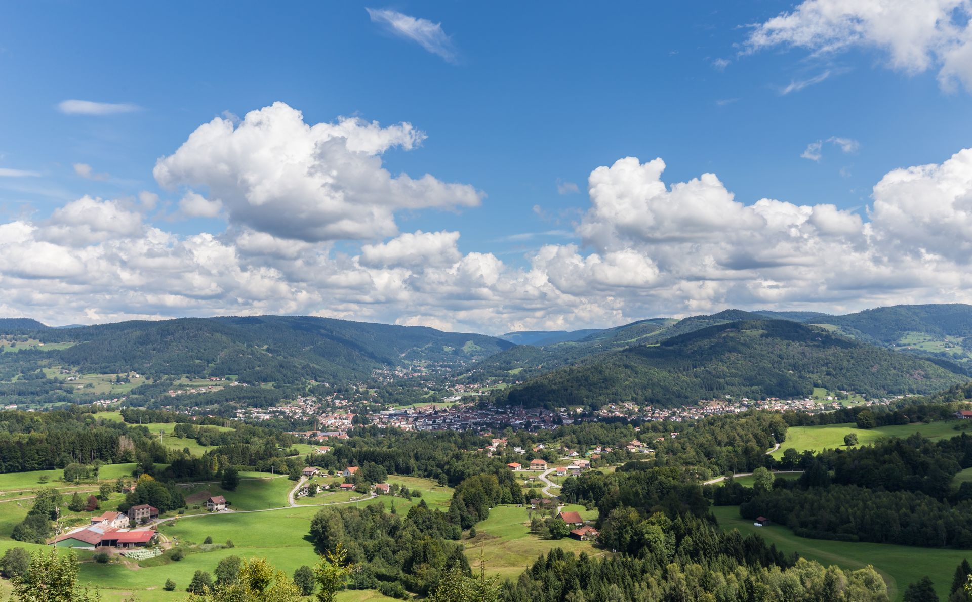 Vue panoramique d'une ville verdoyante dans une vallée, au pied de collines ondulantes.