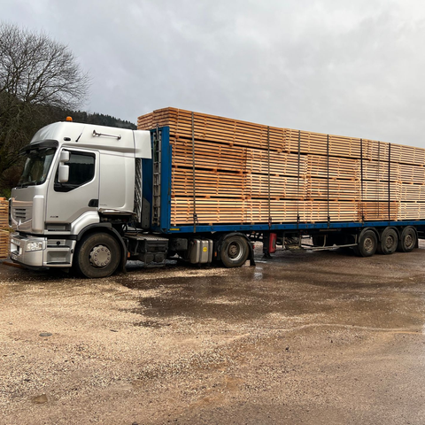 Un semi-remorque blanc transporte une longue cargaison de bois empilé.