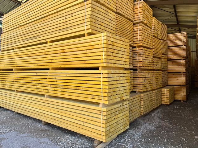 Des piles de planches de bois jaunes entreposées dans un entrepôt.