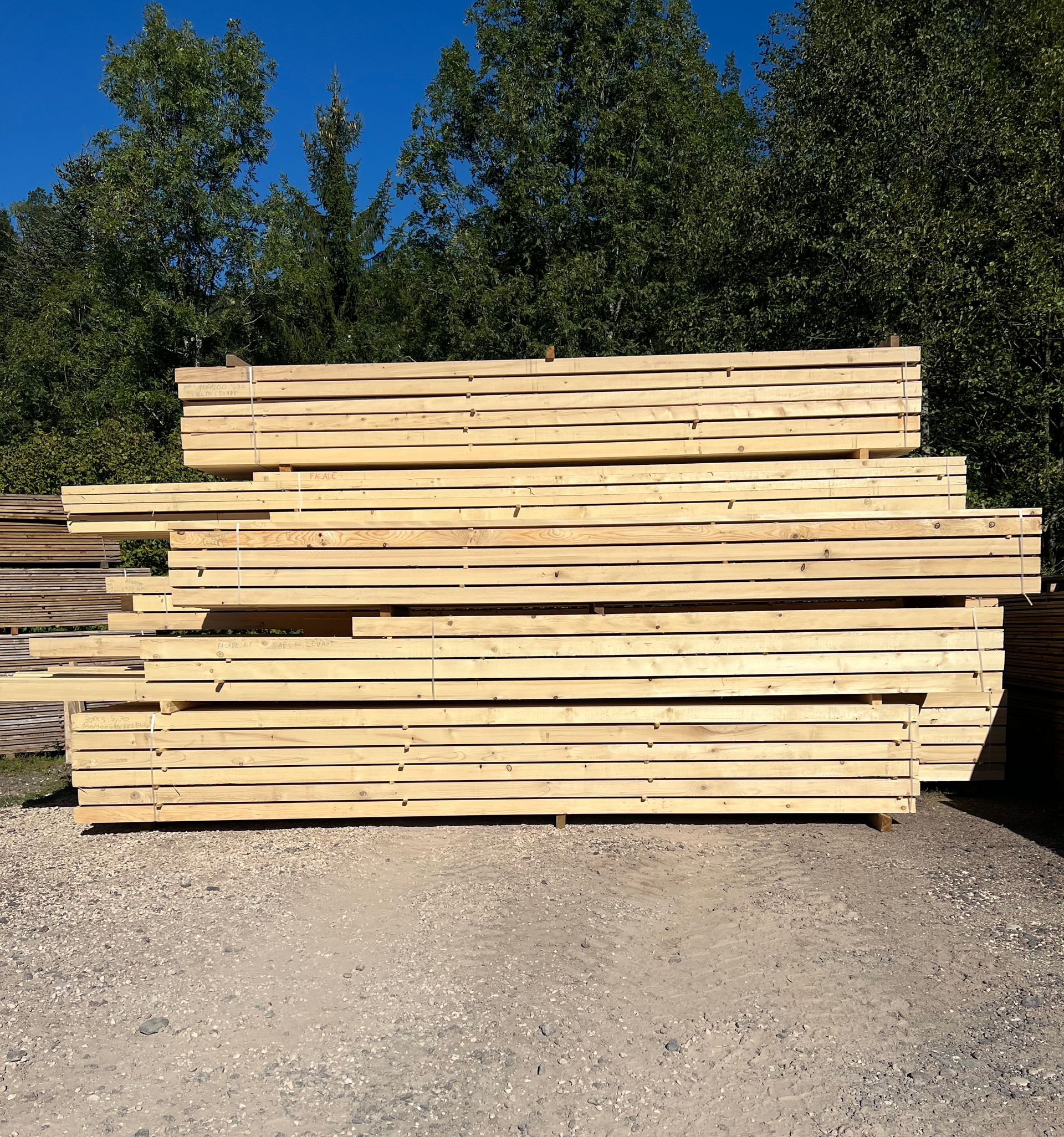 Des piles de bois clair sur du gravier.