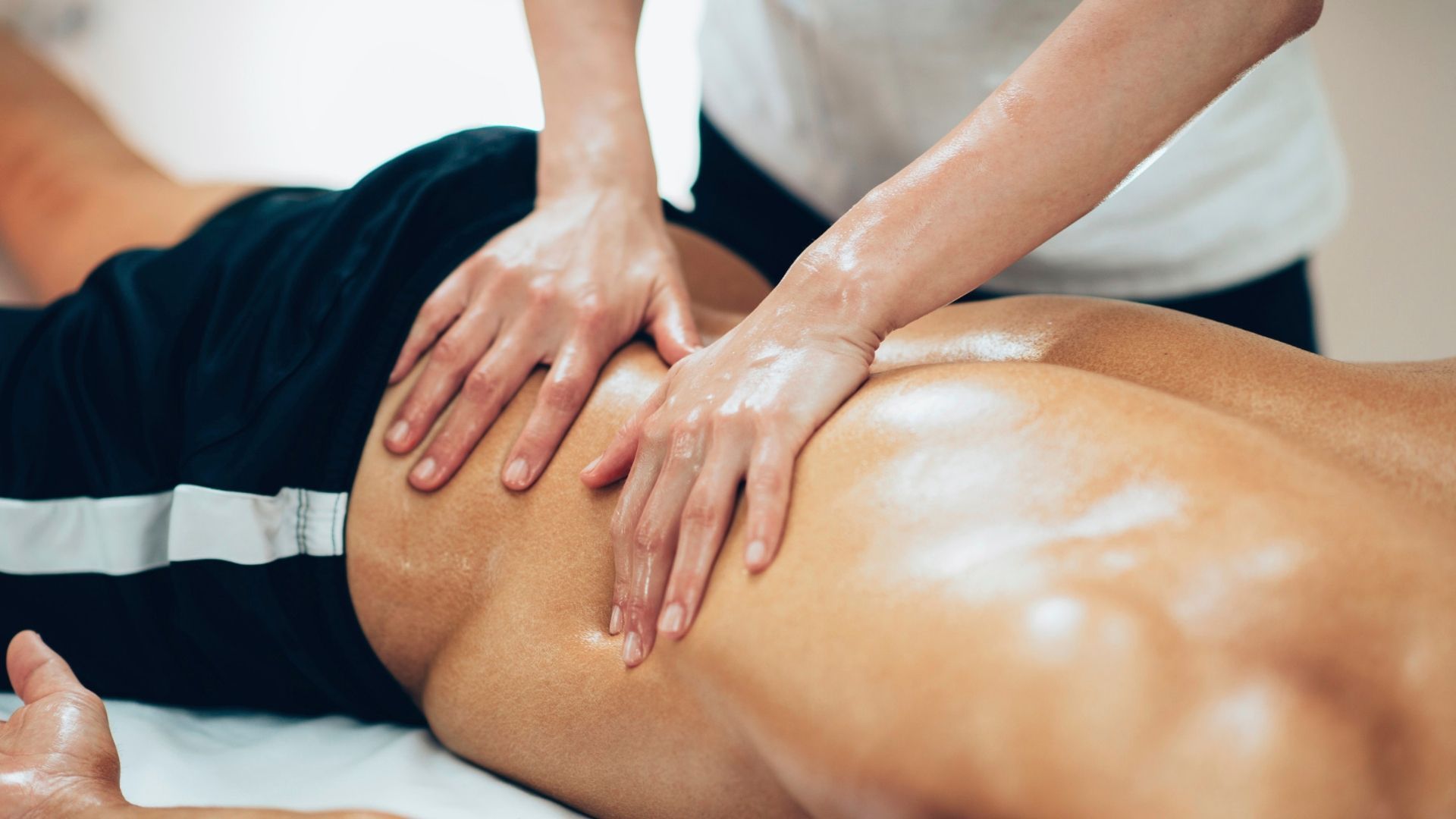 Masajista dando masaje a la parte baja de la espalda y la pierna de una persona.