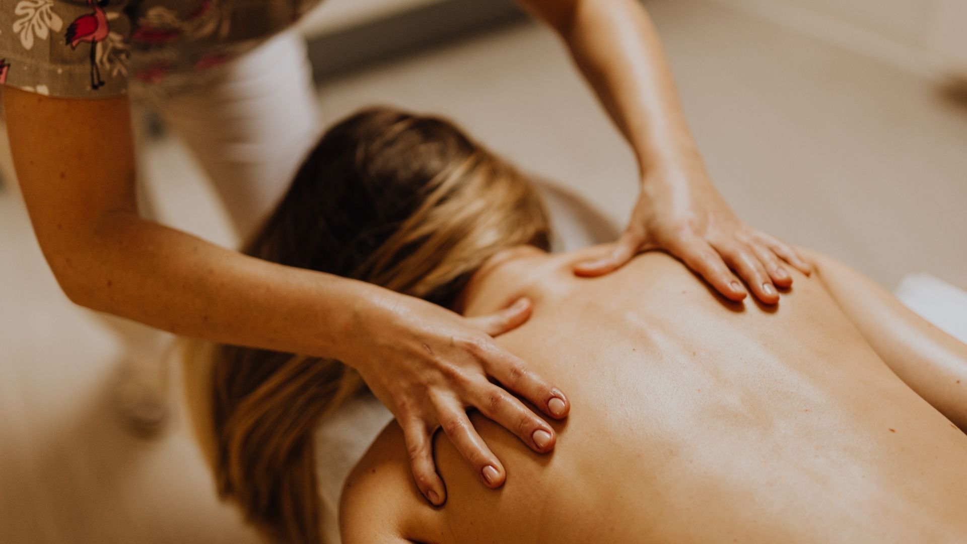 Manos masajeando la espalda de una persona. Se aprecian piel clara y cabello rubio.