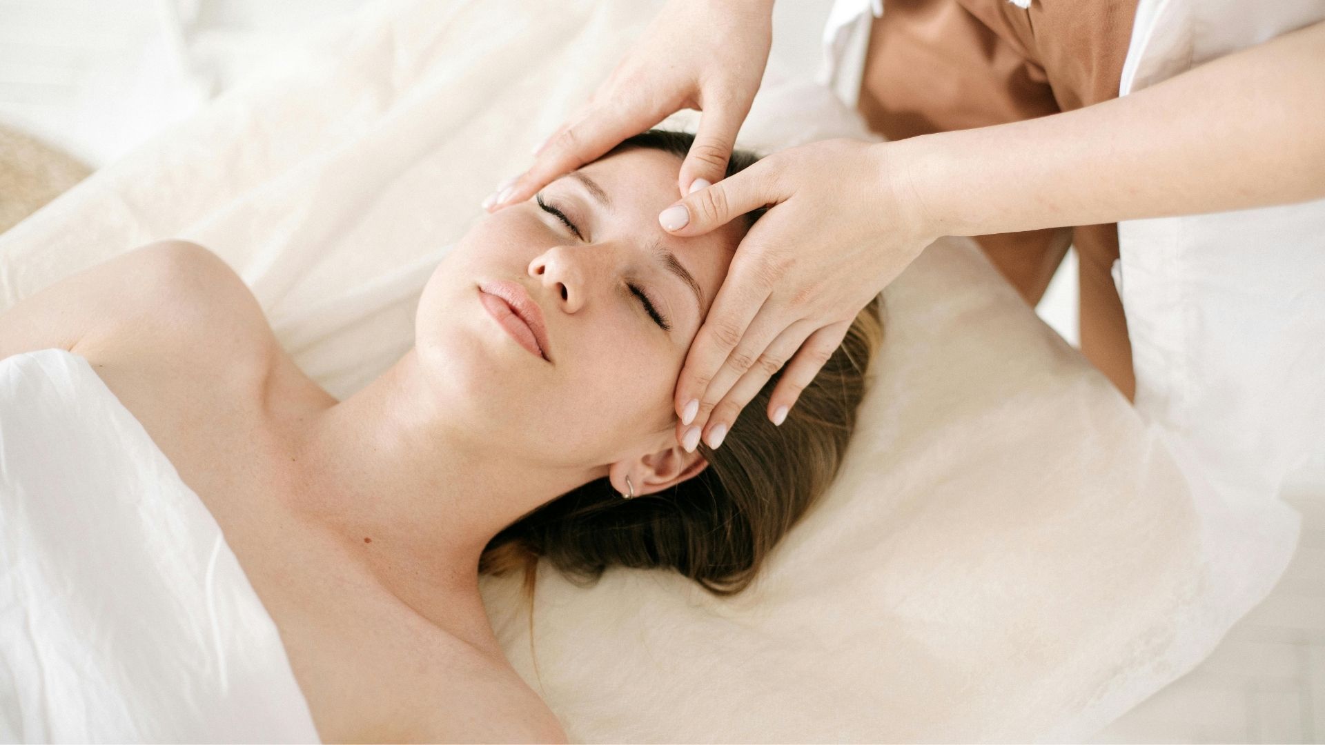 Persona recibiendo un masaje facial con las manos presionando suavemente sobre la frente.